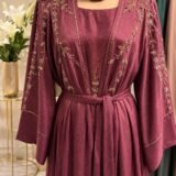Elevate your modest wardrobe with this elegant maroon abaya set, crafted from premium textured fabric with a graceful drape. The design features intricate floral embroidery embellished with delicate beadwork along the front panels, shoulders, and sleeves, adding a refined touch of luxury. The open-front abaya is complemented by a matching inner dress and coordinating hijab, creating a sophisticated and effortless look for special occasions, evening gatherings, weddings, Eid celebrations, and formal events. A matching waist belt allows for adjustable styling and a flattering silhouette.